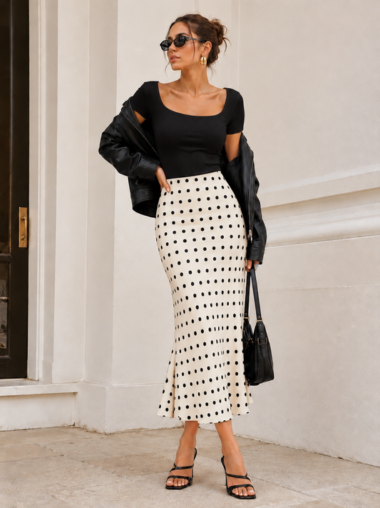White and black polka dot fishtail midi skirt with a fitted silhouette and flowing flared hem, styled as a chic women's printed skirt for a feminine summer outfit with playful Parisian charm.