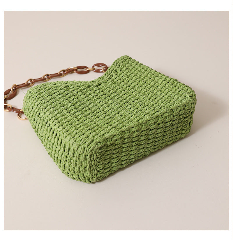 Compact woven straw bag with curved shape and resin chain strap, a lightweight straw shoulder bag designed for beach day bag outfits, summer outings, and relaxed vacation styling.