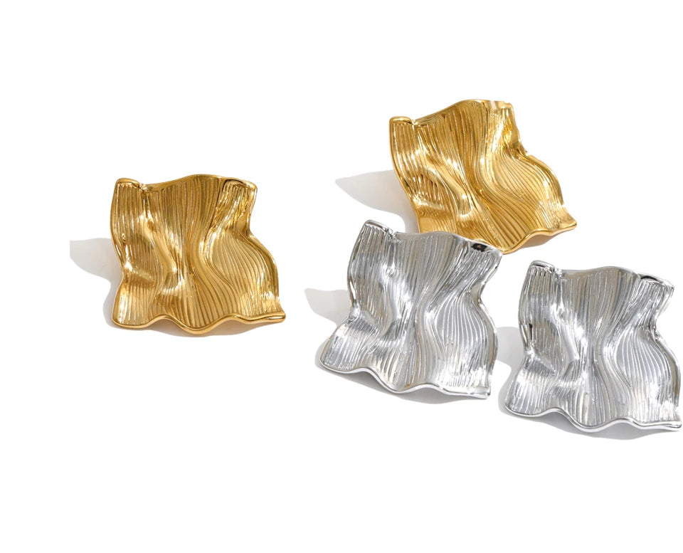Silver square stud earrings in stainless steel with a fluid wavy silhouette, raised vertical grooves and reflective metal surface, designed as contemporary minimalist jewelry for monochrome outfits, office dressing and weekend occasions.