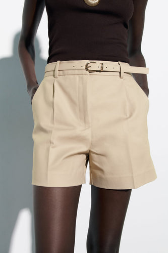 white tailored shorts, shorts with belt, belted shorts, office shorts, ladies tailored shorts, High-waisted wide-leg belted shorts for women, tailored high-waist pleated design, high-waist belted shorts, chic neutral outfit for summer travel, office wear, and effortless brunch styling.