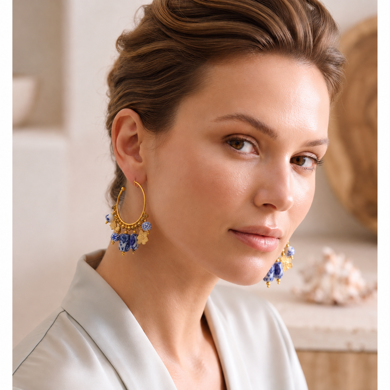 drop hoop earrings with blue ceramic bead accents, floral gold charms. Women's gold plated statement earrings featuring porcelain-inspired ceramic beads, an open hoop design and dangling charm details, perfect for resort wear, occasion dressing and elegant vacation accessories.