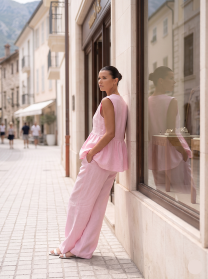 Pink cotton matching set with a feminine peplum silhouette, sleeveless V-neck top, and relaxed trousers, creating an elegant European summer outfit for travel, sightseeing, and sophisticated city style.