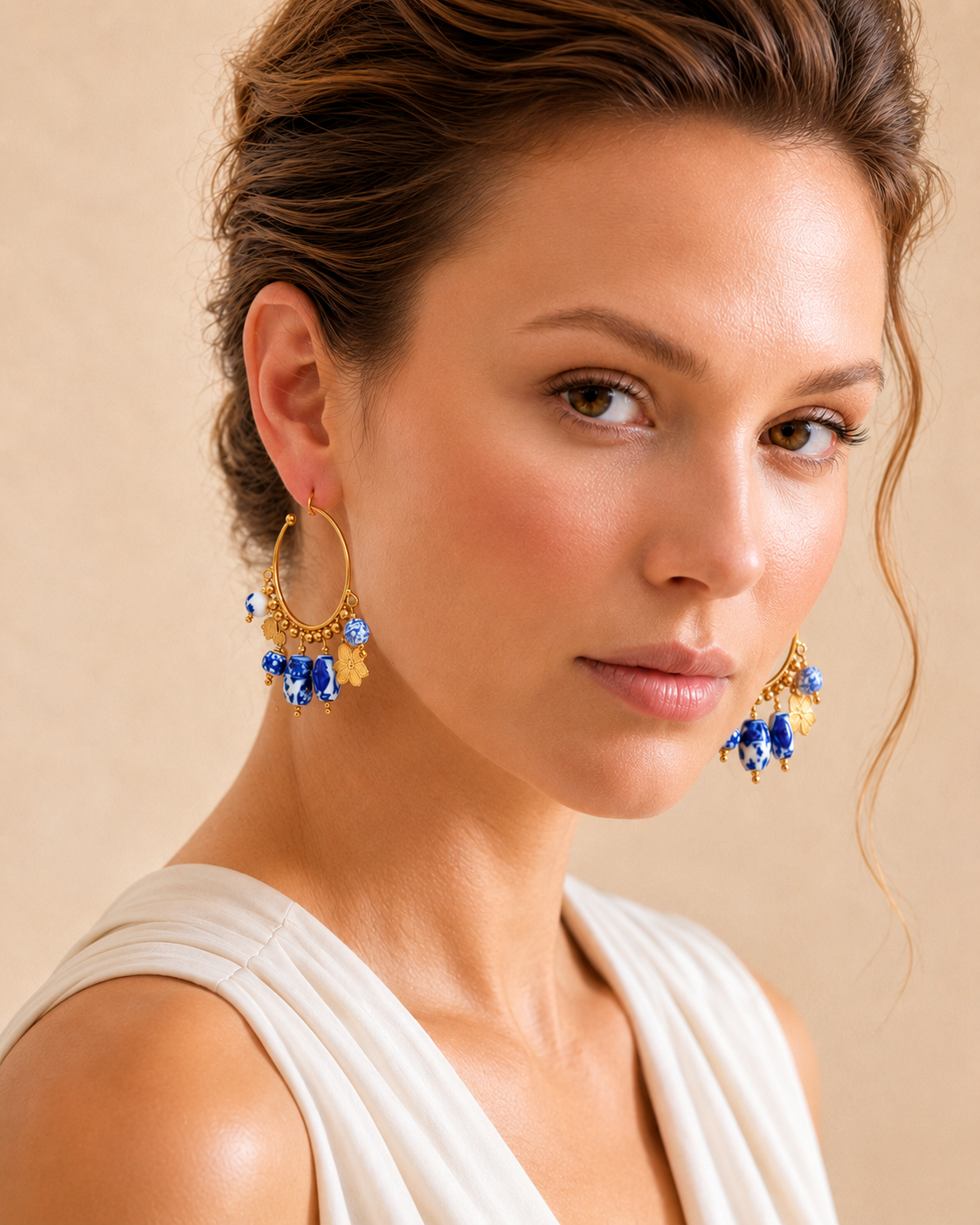 drop hoop earrings with blue ceramic bead accents, floral gold charms. Women's gold plated statement earrings featuring porcelain-inspired ceramic beads, an open hoop design and dangling charm details, perfect for resort wear, occasion dressing and elegant vacation accessories.