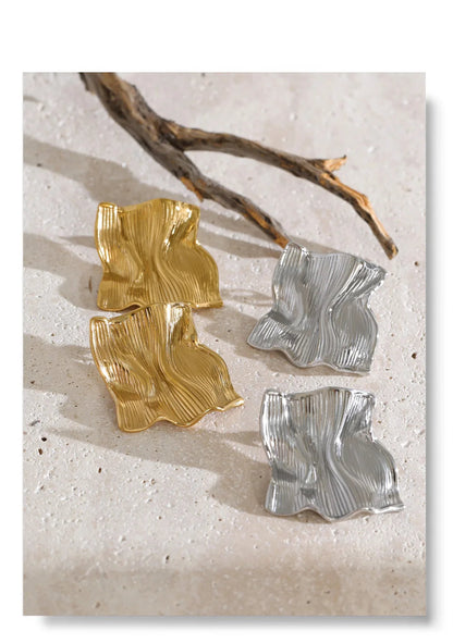 Women's gold and silver textured metal earrings featuring an irregular square silhouette, undulating sculptural folds and polished stainless steel finish, combining geometric statement studs with modern jewelry styling for brunch and evening events.